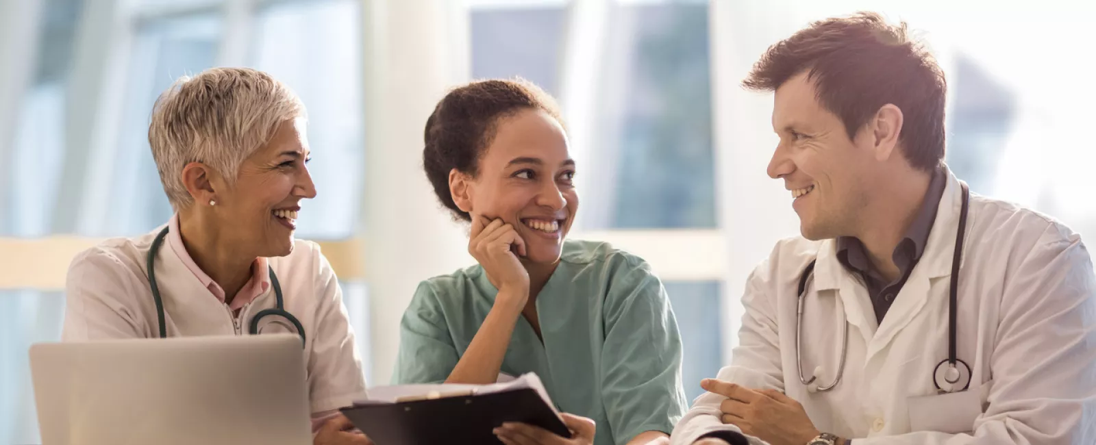 Drei Ärzte sitzend an Tisch, mit Laptop 