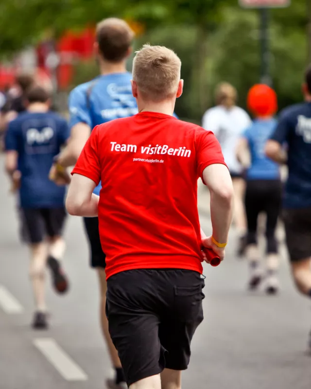 Läufer auf der Straße welche mit Rücken zu Bild sind, ein Läufer mit rotem Shirt, Aufdrucka auf Shirt: Team visitBerlni