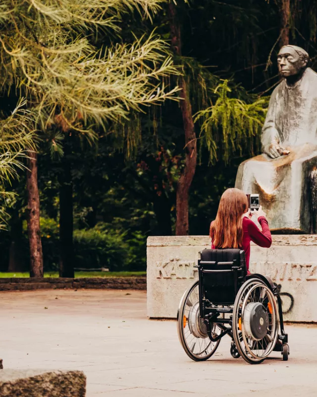 Frau im Rollstuhl fotografiert Statue im Park