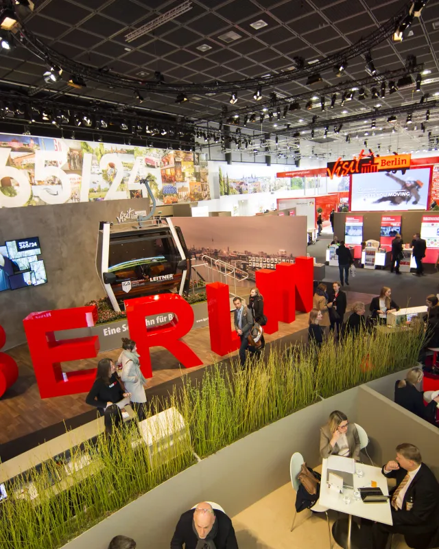 Blick auf ITB Stand, große rote Berlin Buchstaben, Besprechungstische mit Leuten, im Hintergrund eine 365/24 Grafik