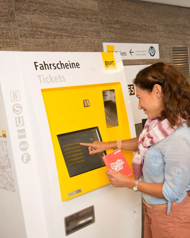Frau mit Berlin WelcomeCard in der Hand an BVG Automat, Automat bedienend