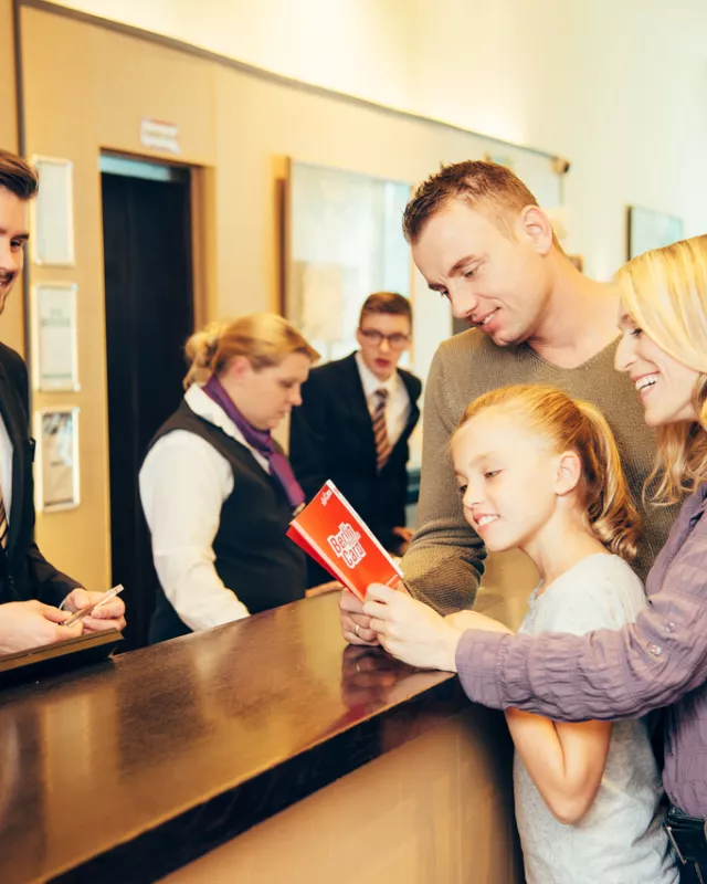 Junge Famliie mit Berlin WelcomeCard Guide an Hotelrezeption. Rezeptionist hinter Rezeption