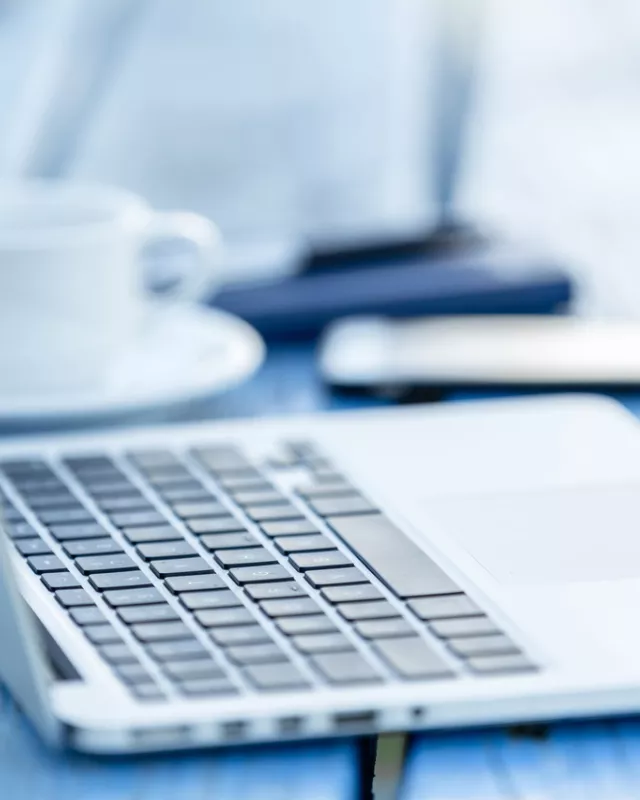 Opened laptop with smartphone, pen and cup of coffee