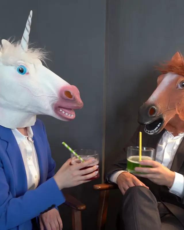 Zwei Menschen in Anzügen mit Pferdemasken auf dem Kopf und Drink in der Hand