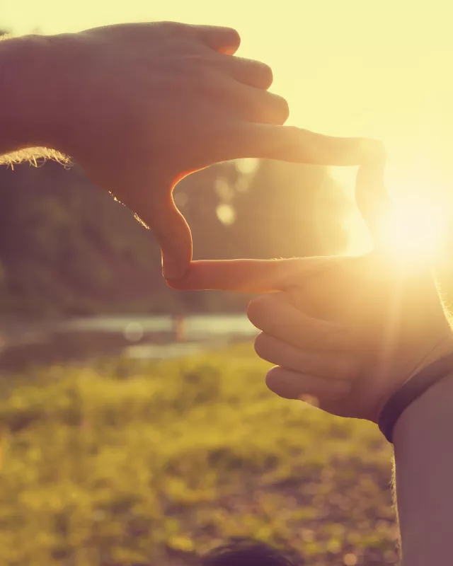Hands framing distant sun rays