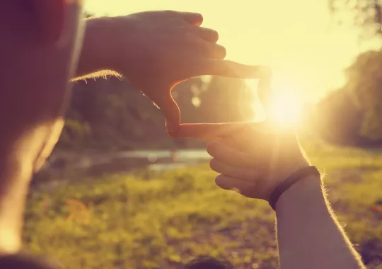 Hands framing distant sun rays