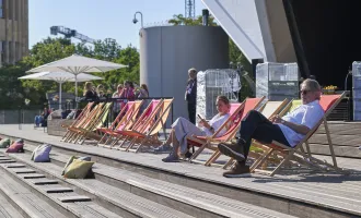 Menschen sitzen auf bunten Liegestühlen vor dem Tempodrom Berlin beim BESTIVAL 2023