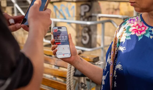 Zwei Personen mit Handys in der Hand, auf dem sichtbaren Display ist die neue App zur Berlin WelcomeCard zu sehen