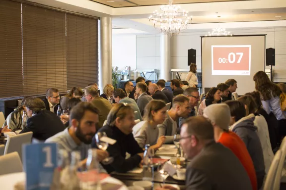 visitBerlin-Business Speed Dating Partner während Speed Dating in Tischreihen, im Hintergrund Countdwohn mit 00:07 Sekunden auf Beamer